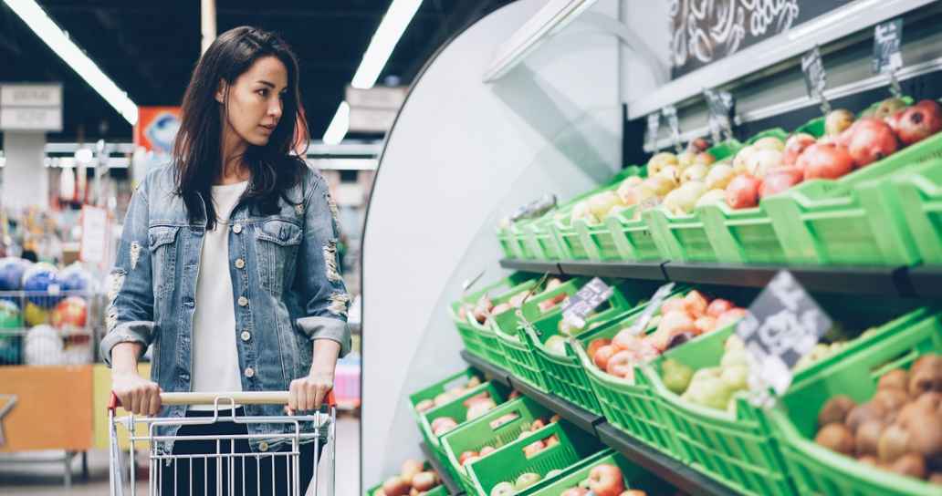 Einkaufende Frau im Supermarkt neben der Gemüseauslage